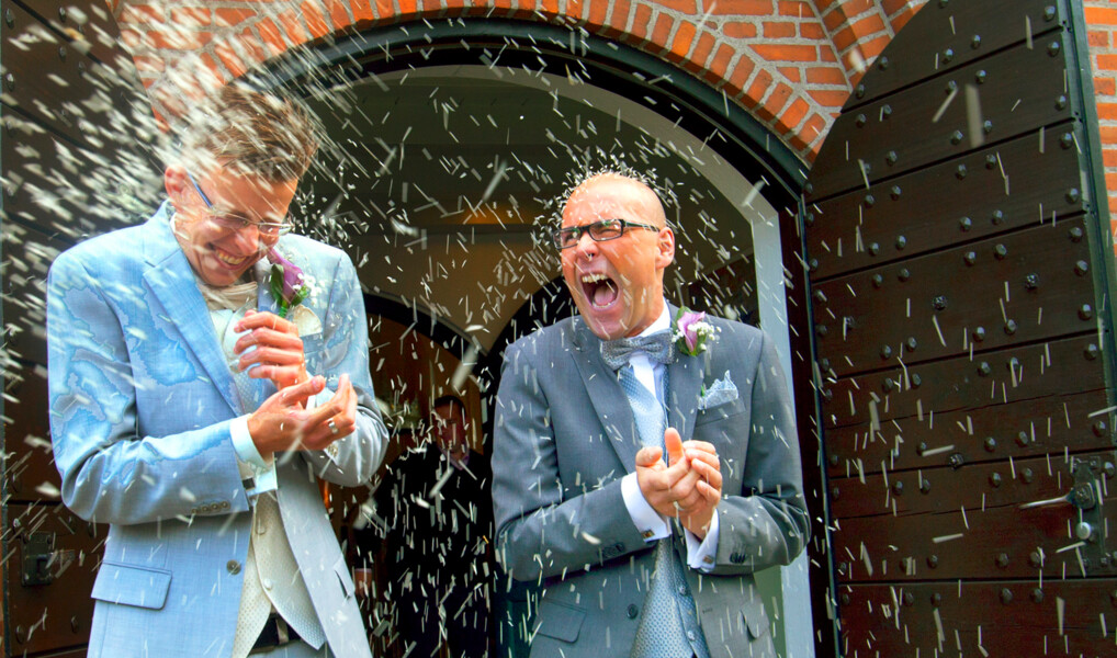 To mænd i jakkesæt får kastet ris på sig foran kirkedøren, lige efter de er blevet gift.