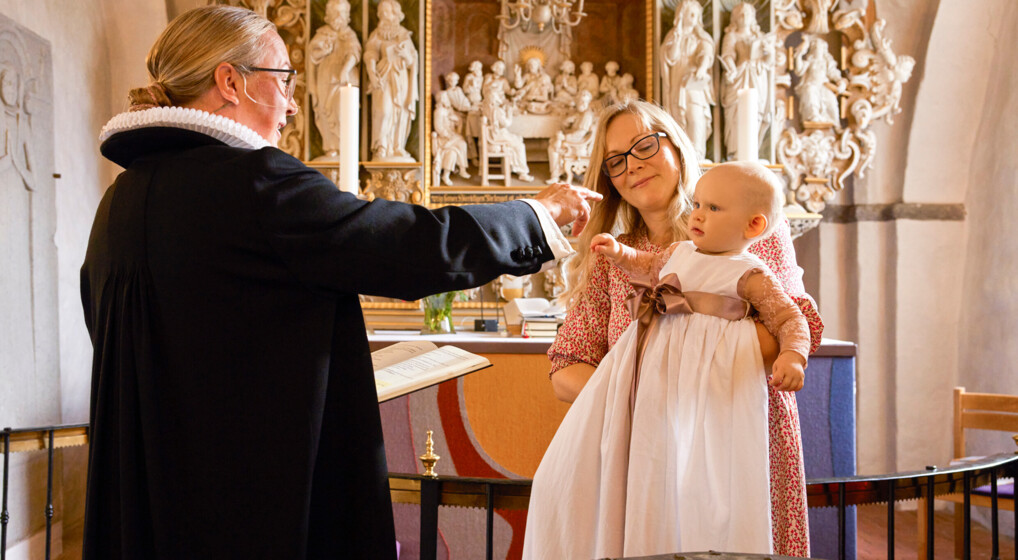 Præst tegner korstegn for ansigtet på et dåbsbarn i lang, hvid dåbskjole