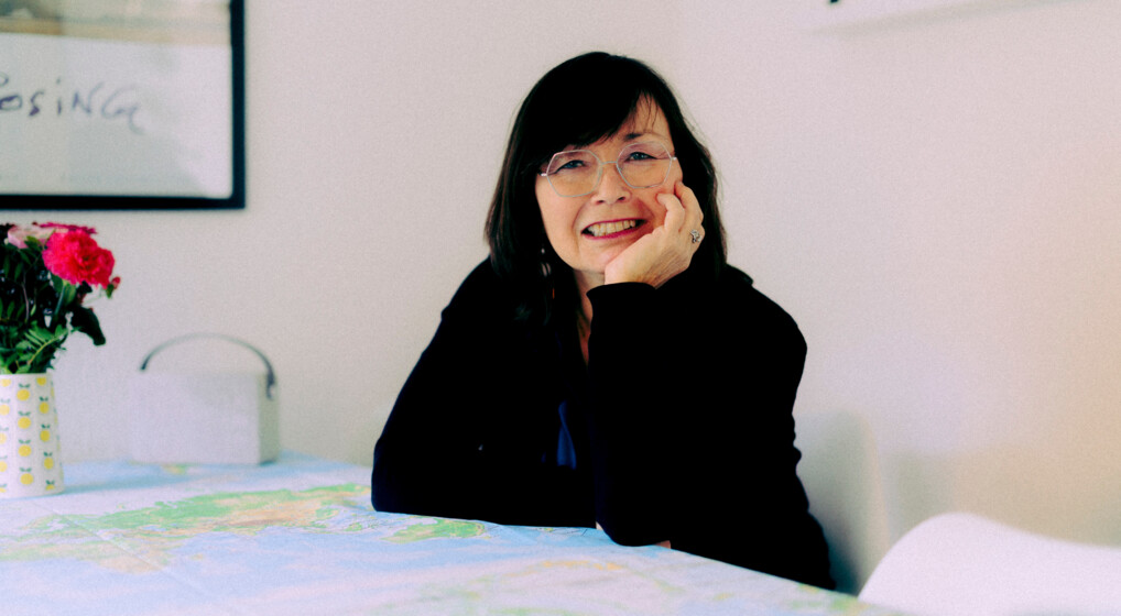 Den grønlandske præst Marianne Krog sidder ved sit spisebord med armene hvilende på et grønlandskort