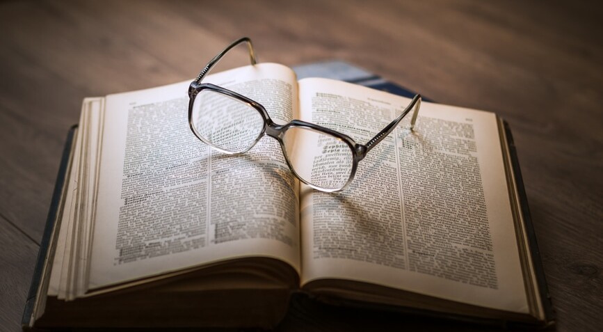 Bibel ligger opslået på et bord med et par læsebriller på