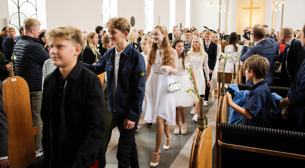 En række glade konfirmander går ned langs midtergangen, efter de er blevet konfirmeret i kirken.