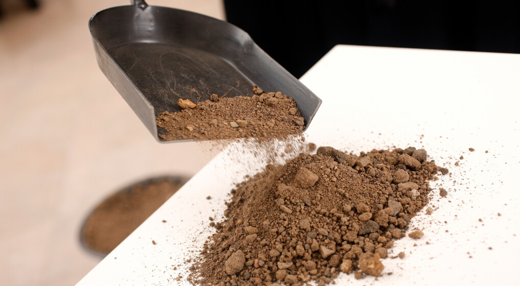 En præst kaster jord på en hvid kiste med en lille håndskovl ved en bisættelse.