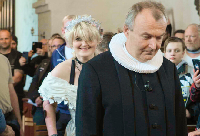 En konfirmand er på vej op af midtergangen i kirken, imens præsten går foran hende.