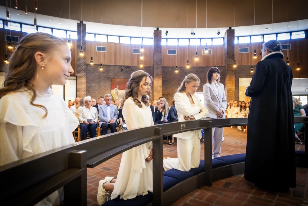 4 konfirmander er samlet foran alteret i en kirke, hvor præsten er i gang med at tale til konfirmanderne.