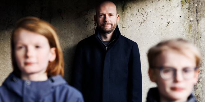 Brian Nørremark står op ad en mur mens hans to sønner ses slørrede i forgrunden